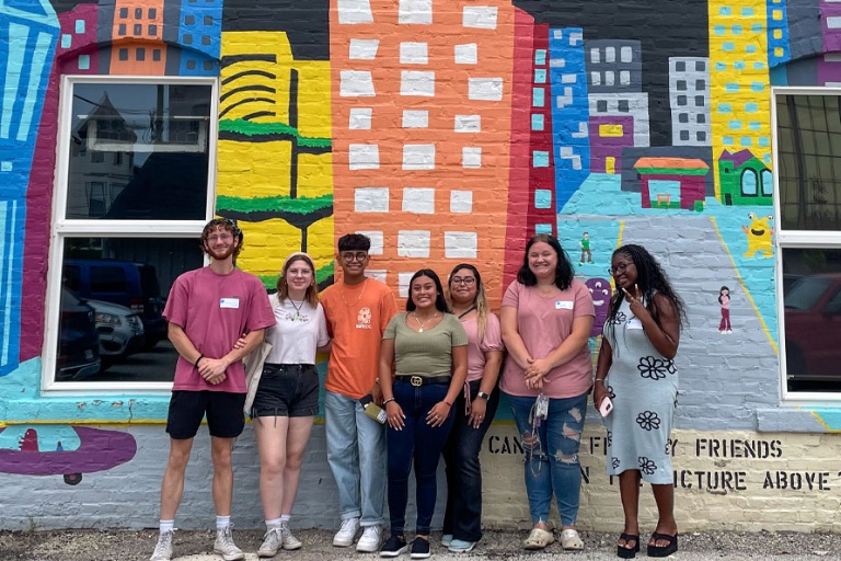 Students standing in front of a colorful mural.