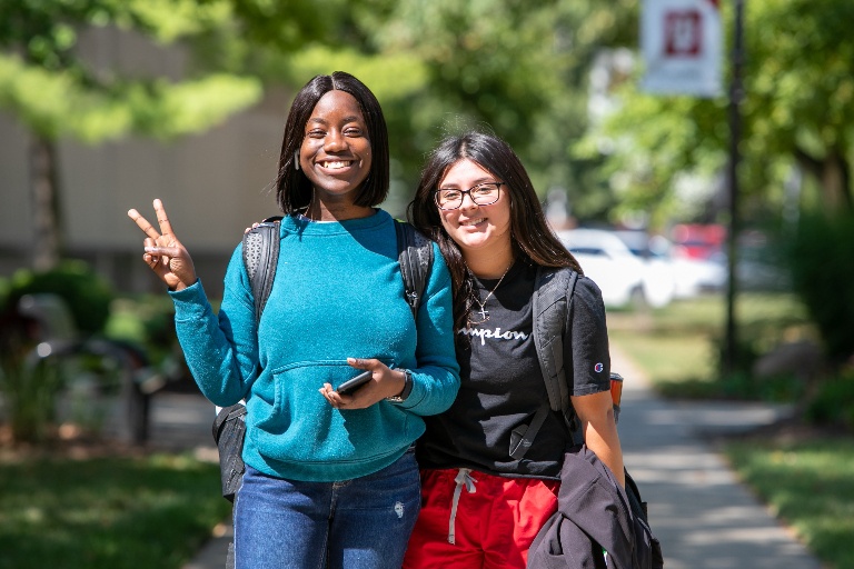 Two students smiling outdoor, holding up a peace sign.