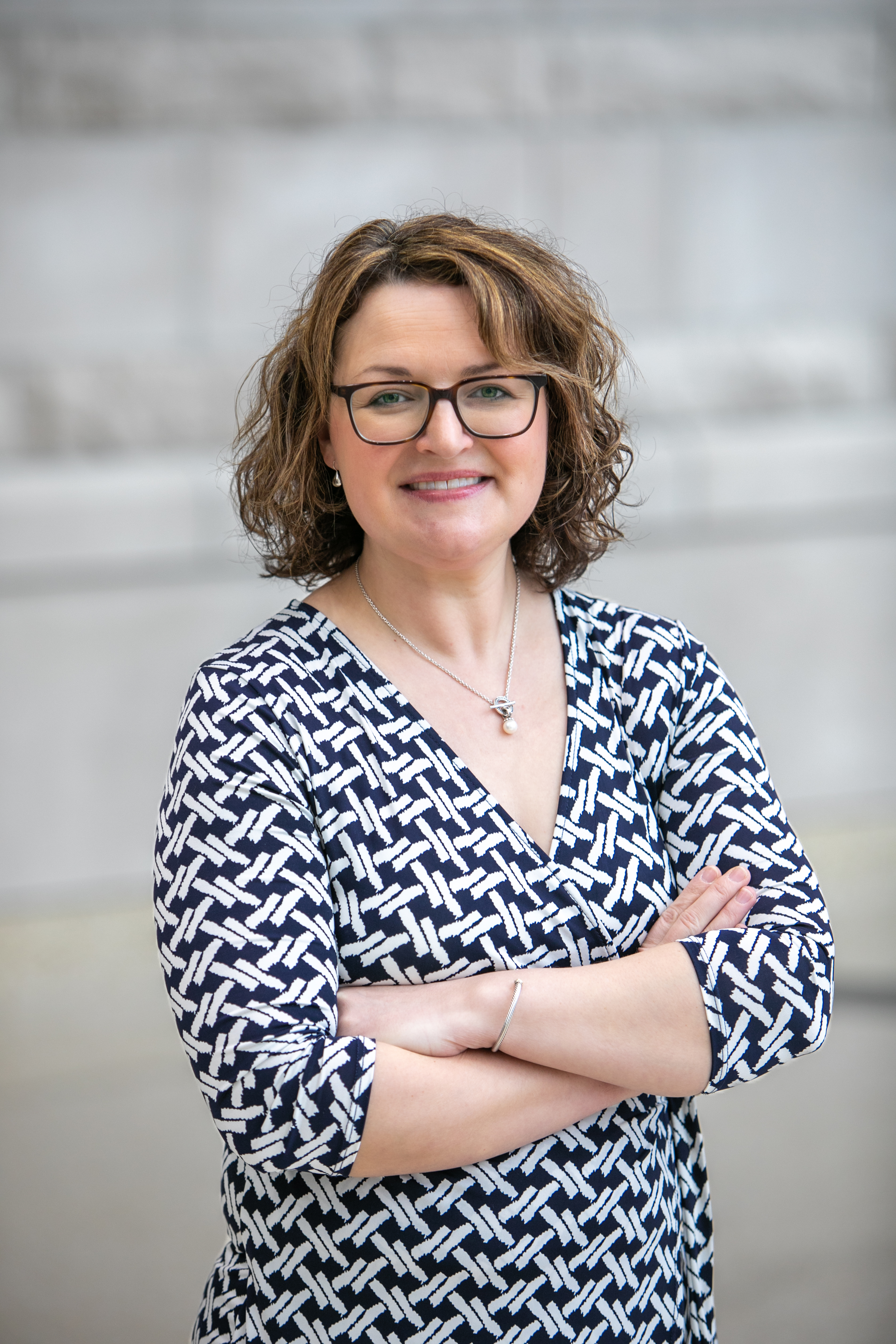 Image of a woman with short curly hair and glasses, wearing a black and white dress, smiling at the camera. 