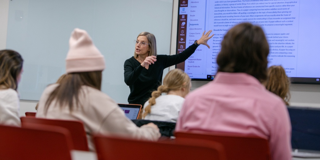 A teacher pointing to a screen in a room full of students