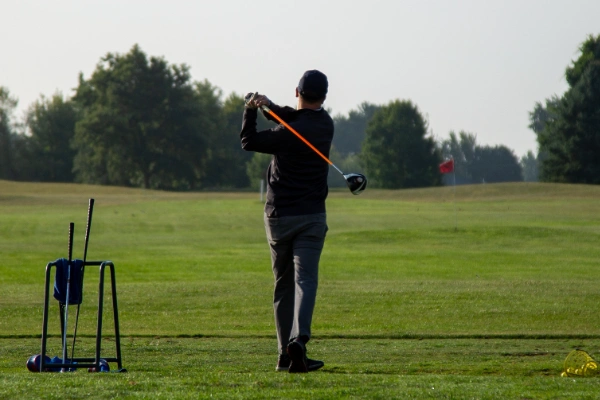 A man holds a golf club while looking into the distance.