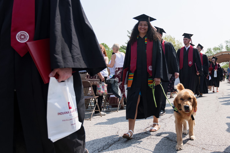 An IUK graduate walks in the processional with her service dog