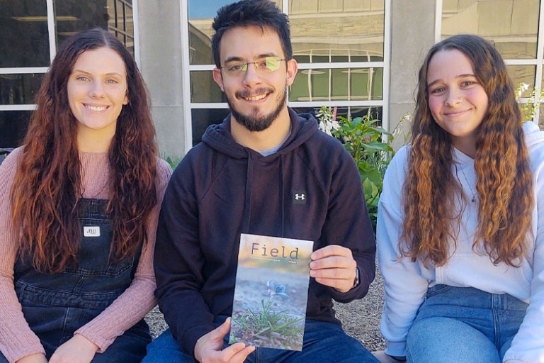 Three student interns sitting outdoor, one holding Field magazine.