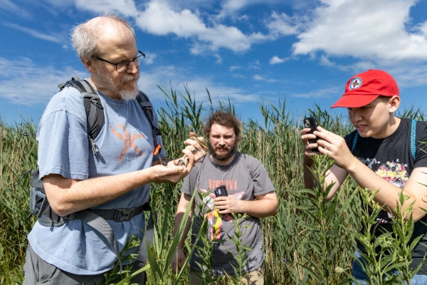 Two men observe a man holding a small snake.