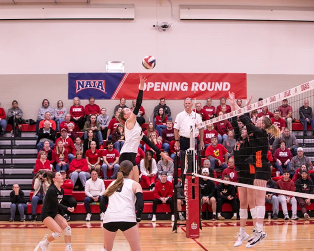 A woman jumps in the air to hit a volleyball. 