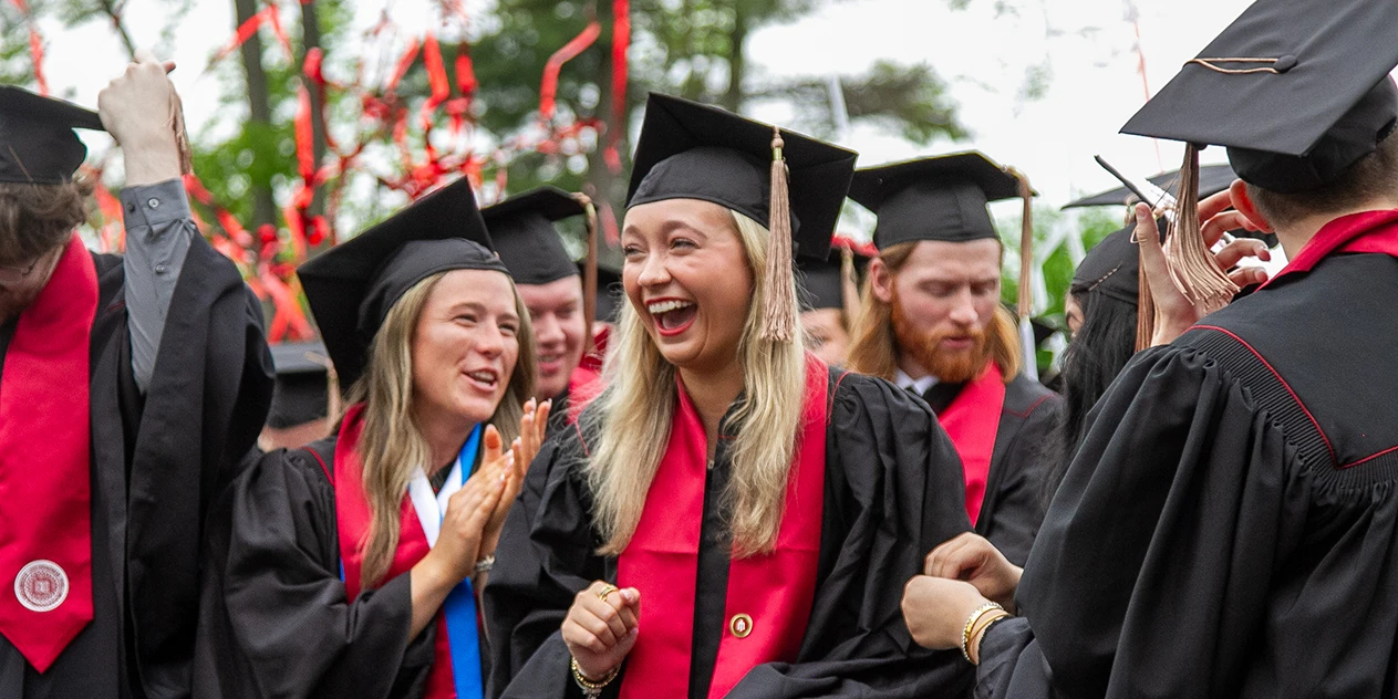 A group of men and women in graduation caps and gowns celebrate. 