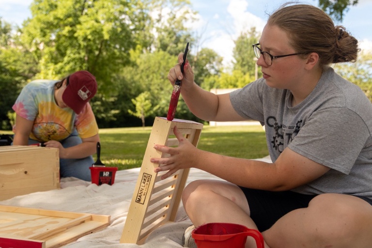 Two students outdoor painting bee houses.